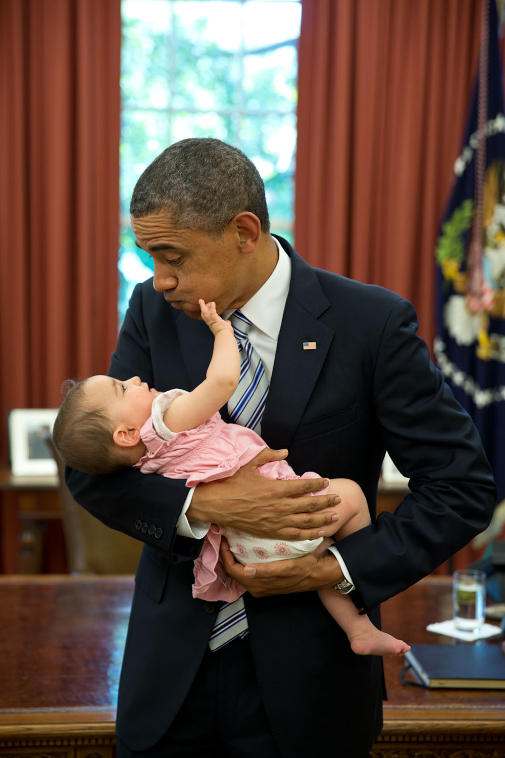 June 14, 2013 "The President had invited departing staff member Adam Neufeld to the Oval Office for a farewell photograph. When the President picked up Neufeld's six-month-old daughter, she started grabbing his face." (Official White House Photo by Pete Souza) This official White House photograph is being made available only for publication by news organizations and/or for personal use printing by the subject(s) of the photograph. The photograph may not be manipulated in any way and may not be used in commercial or political materials, advertisements, emails, products, promotions that in any way suggests approval or endorsement of the President, the First Family, or the White House.