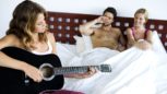 Young couple in bed listening to woman playing guitar