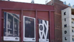 Die Ostfassade des KINDL - Zentrmu für zeitgenössische Kunst in rotem Backstein mit drei Plakaten der aktuellen Ausstellungen.